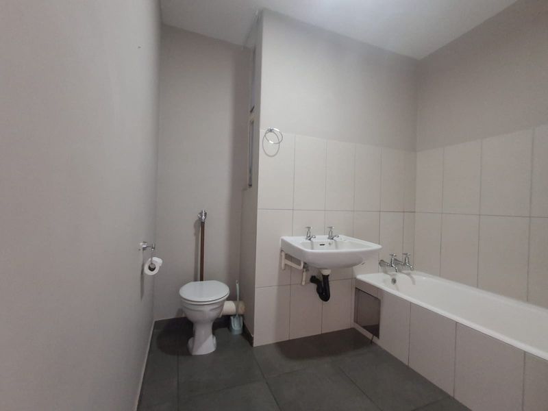 A functional bathroom featuring a wall-mounted basin, bathtub, and toilet with neutral wall and floor tiling.