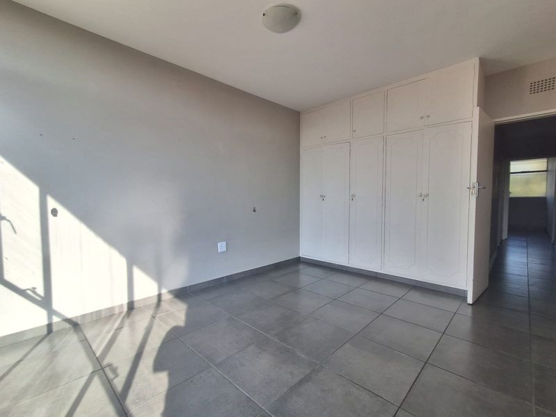 An empty bedroom featuring neutral tiled flooring and ample built-in cupboard storage, offering a clean and versatile space.