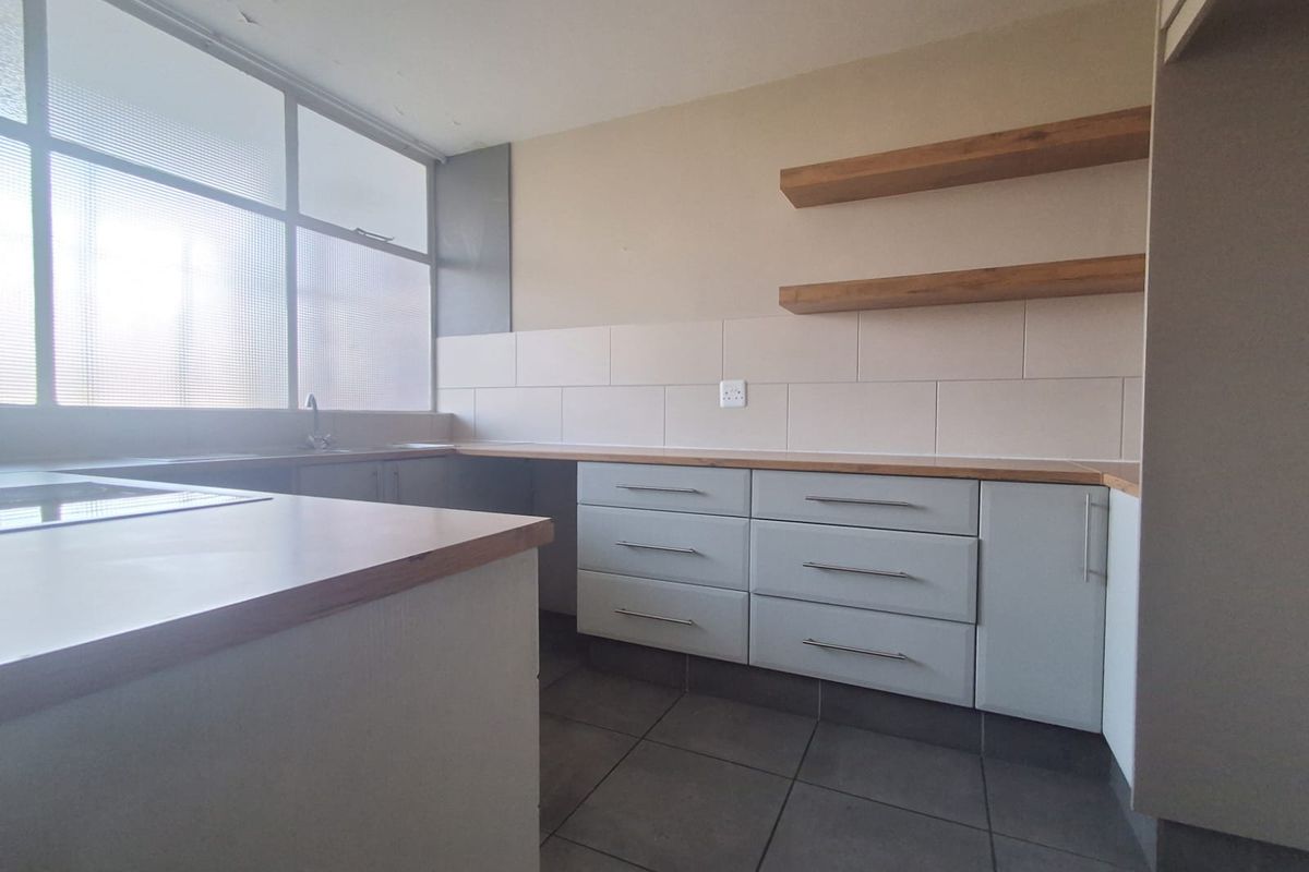 A functional kitchen featuring light grey cabinetry, wooden countertops, floating shelves, and tiled flooring, offering a clean and neutral space for culinary activities.