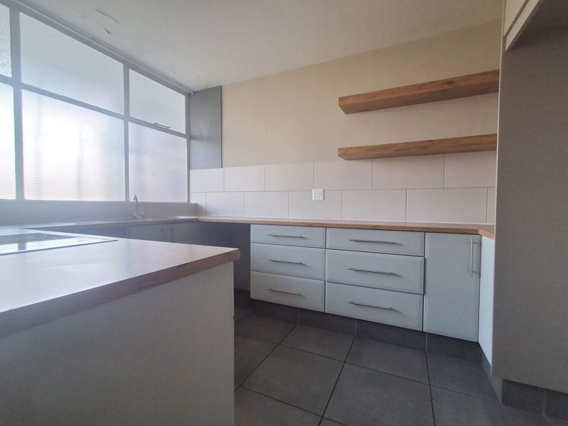 A functional kitchen featuring light grey cabinetry, wooden countertops, floating shelves, and tiled flooring, offering a clean and neutral space for culinary activities.