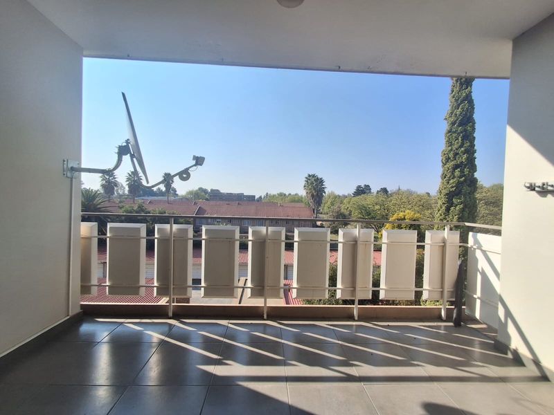 A covered balcony featuring tiled flooring and a metal balustrade, offering an open view of the surrounding neighborhood.