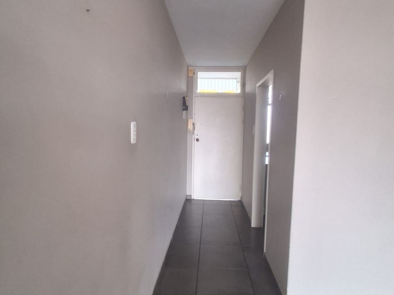 A clean, empty hallway featuring neutral wall tones and dark tiled flooring, leading to an internal door with a transom window.