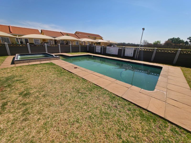 Communal swimming pool and spa area featuring paved surrounds, lawn, and secure precast concrete boundary walling within the townhouse complex.