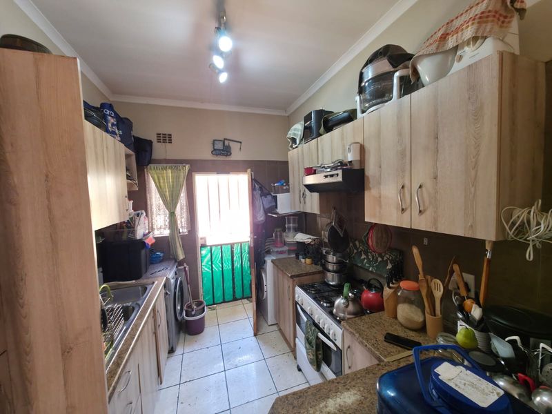 Compact kitchen featuring wood-look cabinetry, granite countertops, gas hob, and direct access to an exterior area through a security gate.