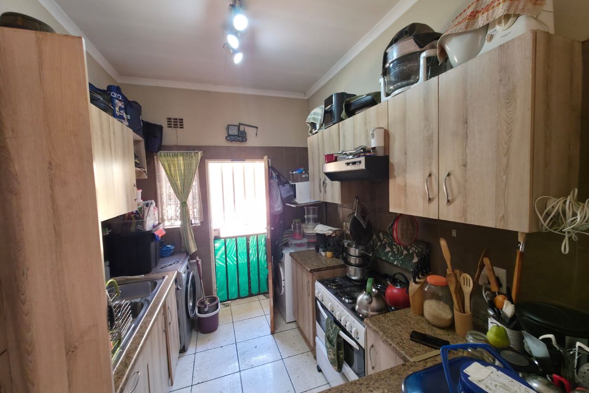 Compact kitchen featuring wood-look cabinetry, granite countertops, gas hob, and direct access to an exterior area through a security gate.