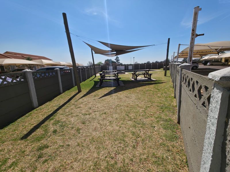 A communal garden area featuring a lawn, precast concrete boundary walls, and overhead shade sails for outdoor seating.