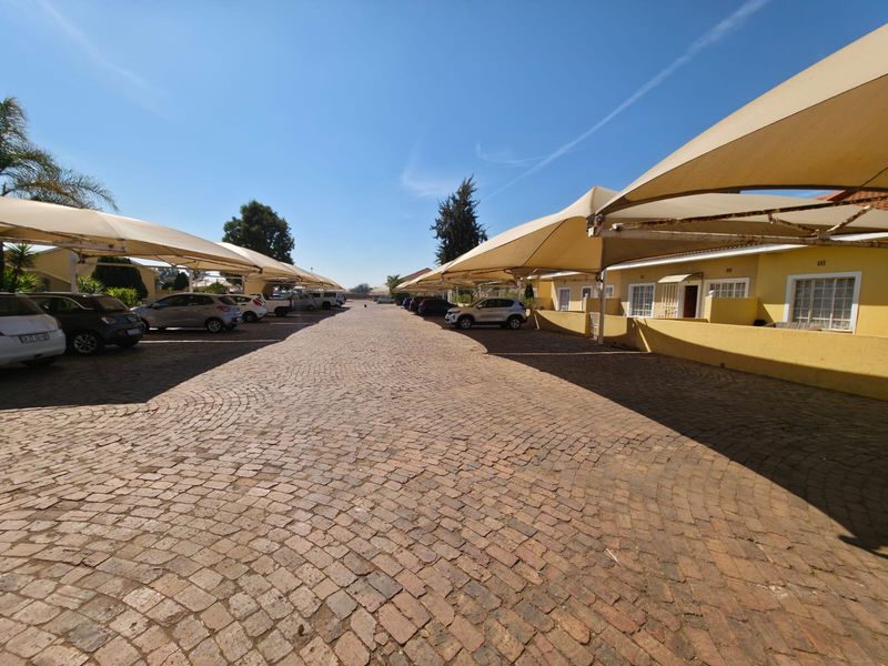 Exterior view of a townhouse complex featuring a paved cobblestone driveway with covered shade cloth parking bays and low-walled residential units.