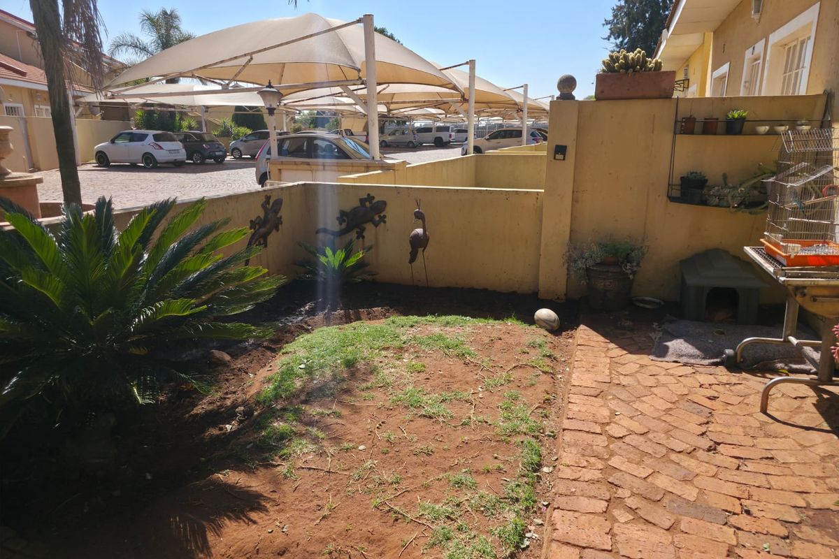A small rear courtyard area featuring brick paving and a patch of lawn, adjacent to a communal parking area with shade cloth carports.