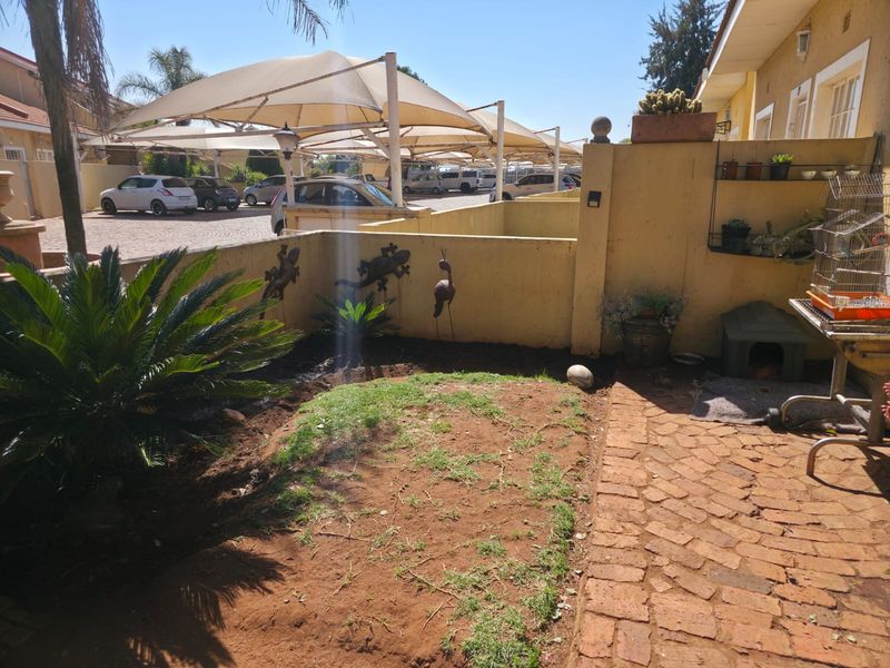 A small rear courtyard area featuring brick paving and a patch of lawn, adjacent to a communal parking area with shade cloth carports.