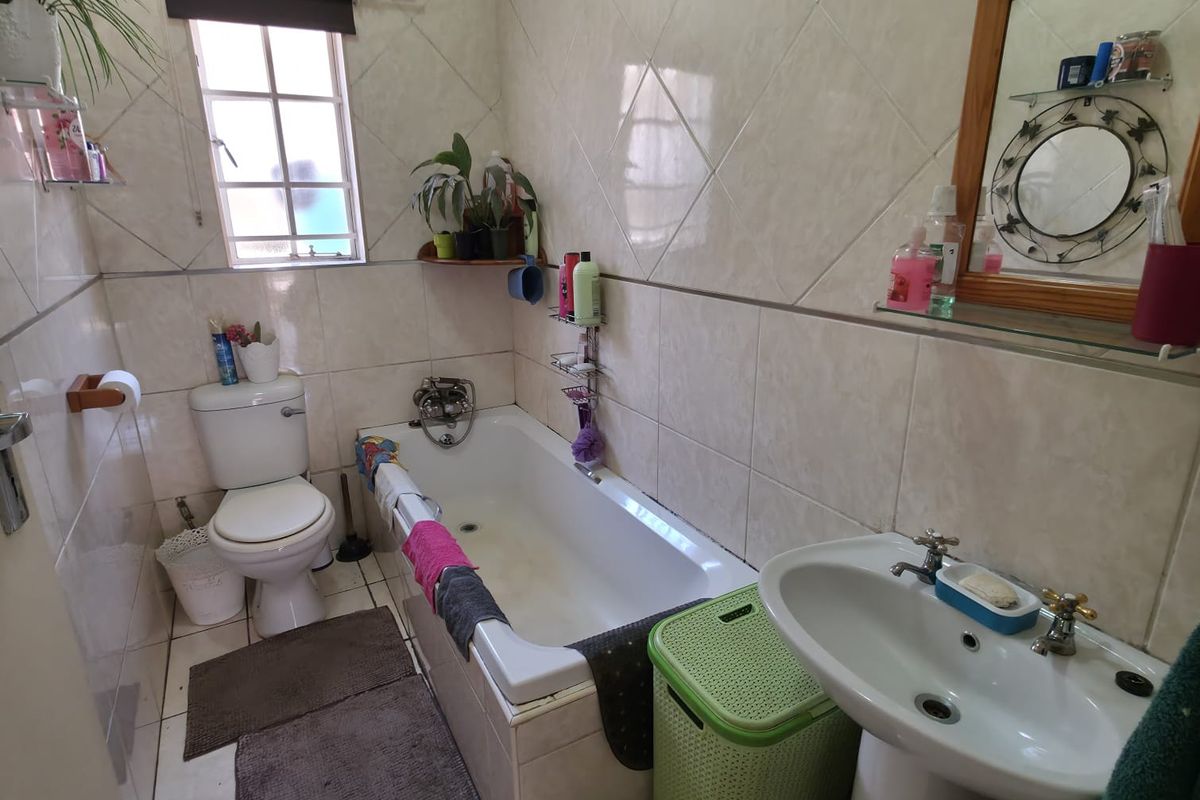 A functional bathroom featuring a bathtub, pedestal basin, and toilet with neutral ceramic wall and floor tiling.