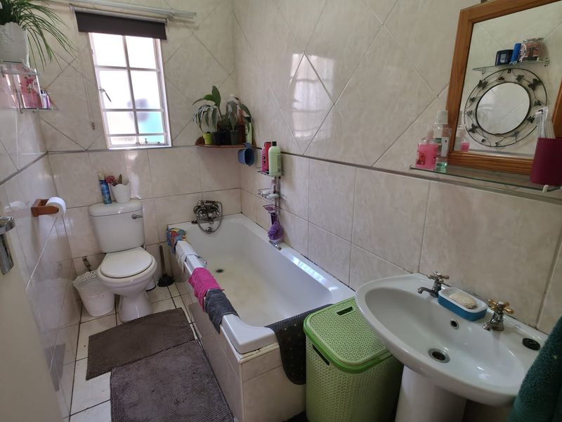 A functional bathroom featuring a bathtub, pedestal basin, and toilet with neutral ceramic wall and floor tiling.