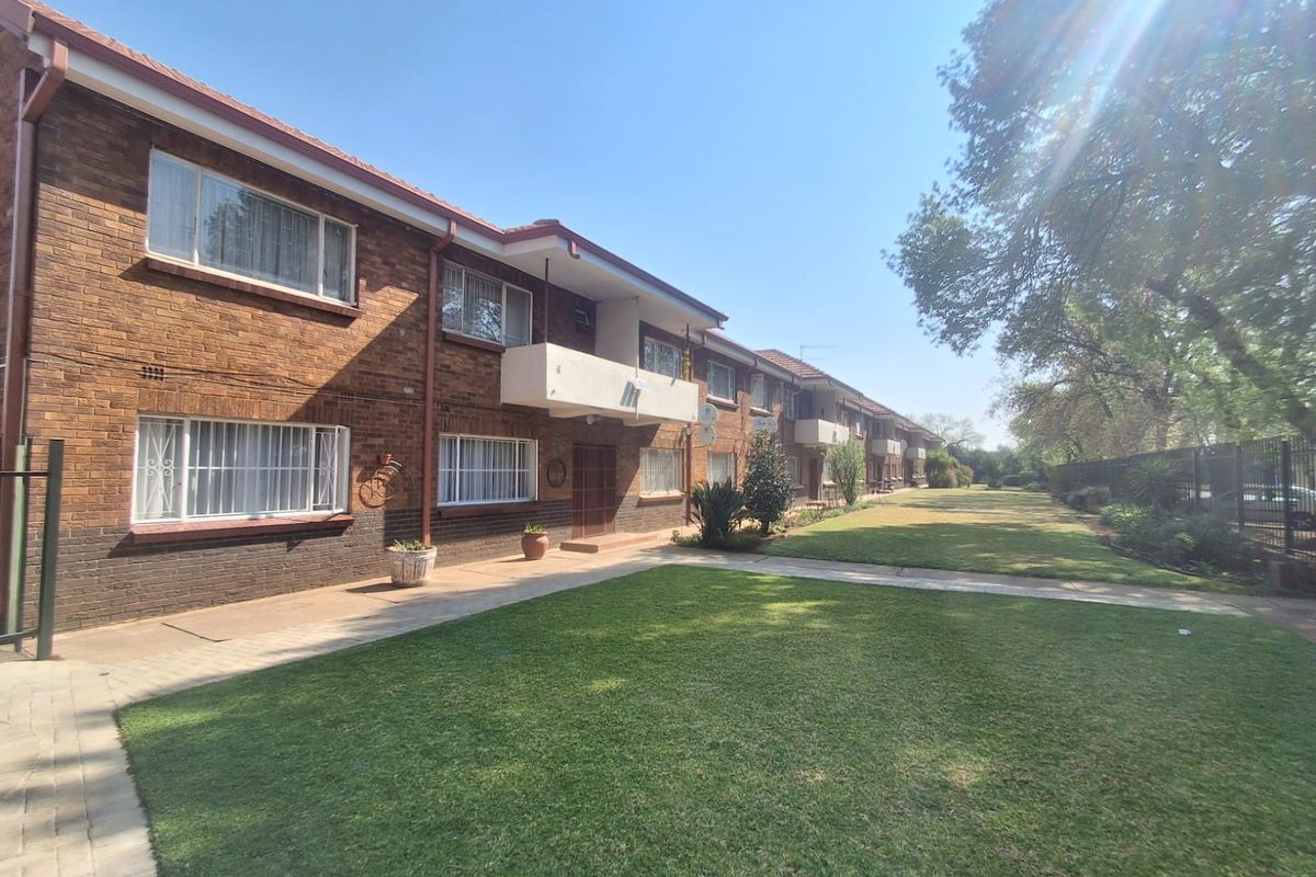 A view of the rear exterior of the flat complex, featuring brick facade, balconies, and a well-maintained communal lawn area.