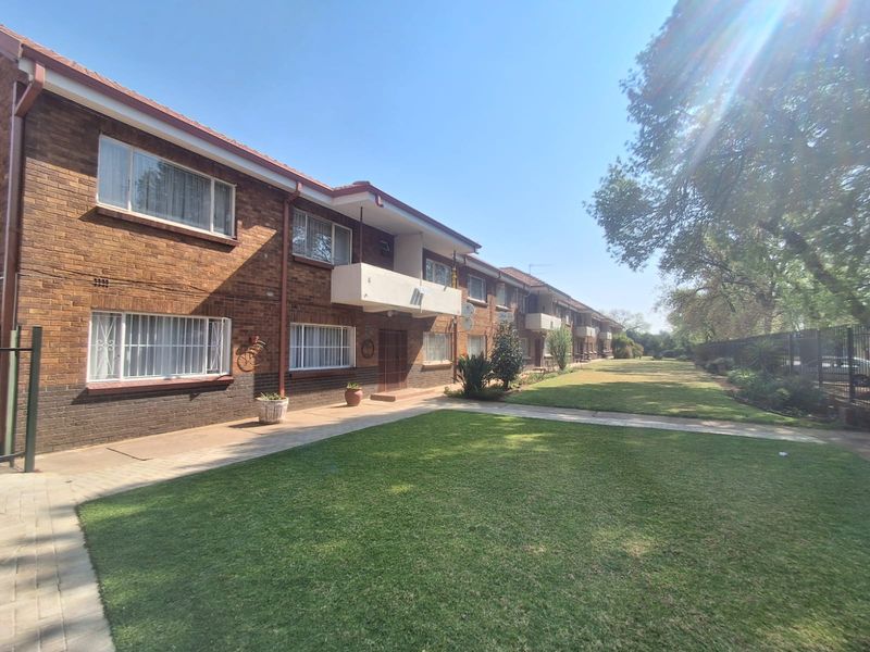 A view of the rear exterior of the flat complex, featuring brick facade, balconies, and a well-maintained communal lawn area.