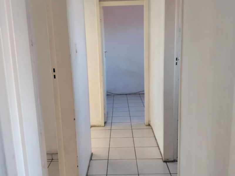 A simple, empty hallway featuring white walls and tiled flooring, providing access to adjacent rooms within the flat.