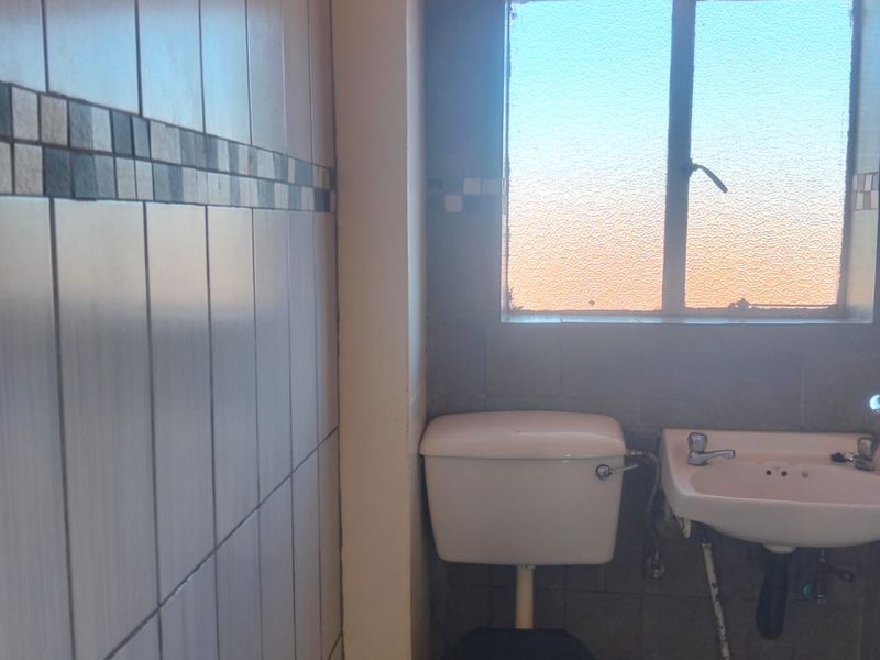 A functional bathroom featuring a toilet, wall-mounted washbasin, and tiled finishes, illuminated by natural light through an obscured glass window.