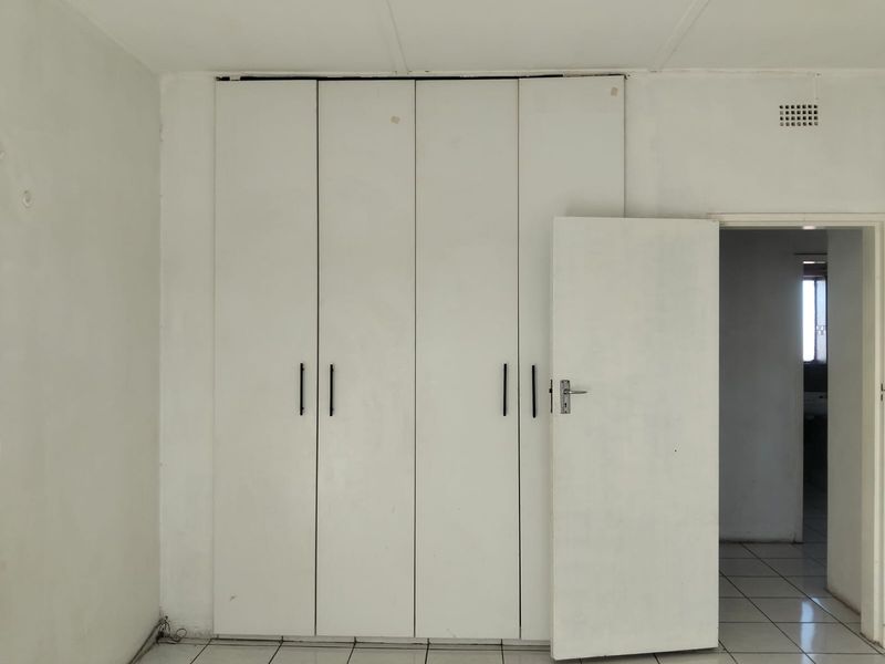 A vacant bedroom featuring white built-in cupboards and tiled flooring, offering a blank canvas for potential interior updates.
