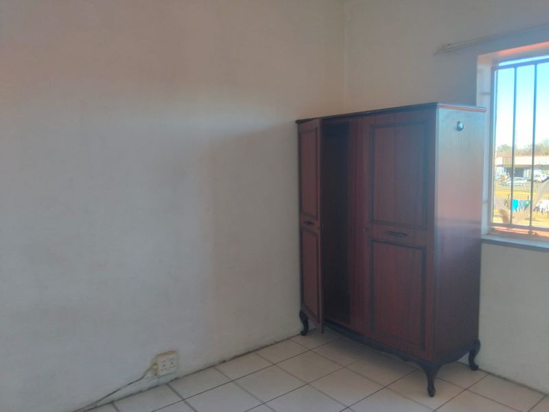A bedroom featuring tiled flooring and a window with security bars, requiring minor cosmetic updates to the wall finishes.