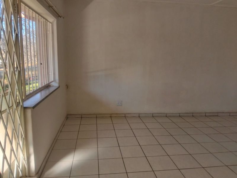 An empty living area featuring tiled flooring, a window with a security gate, and neutral walls, offering a blank canvas for interior design.