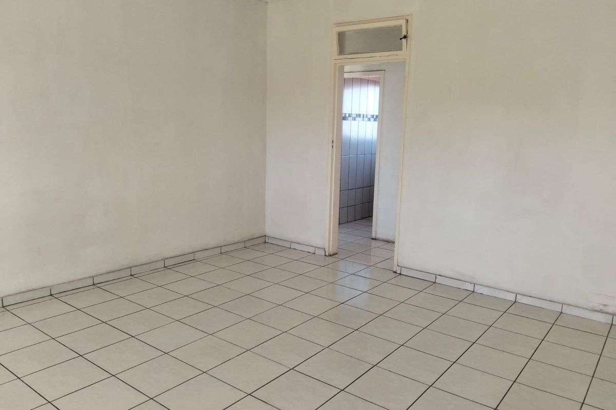 An empty living area featuring white walls and neutral ceramic floor tiles, leading through a doorway into an adjacent tiled space.
