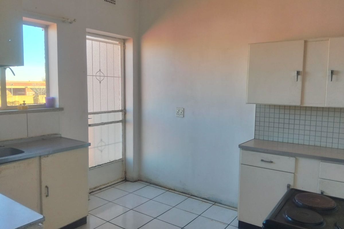 A functional, empty kitchen featuring built-in cabinetry, tiled flooring, and a tiled backsplash, with direct access to an exterior door.