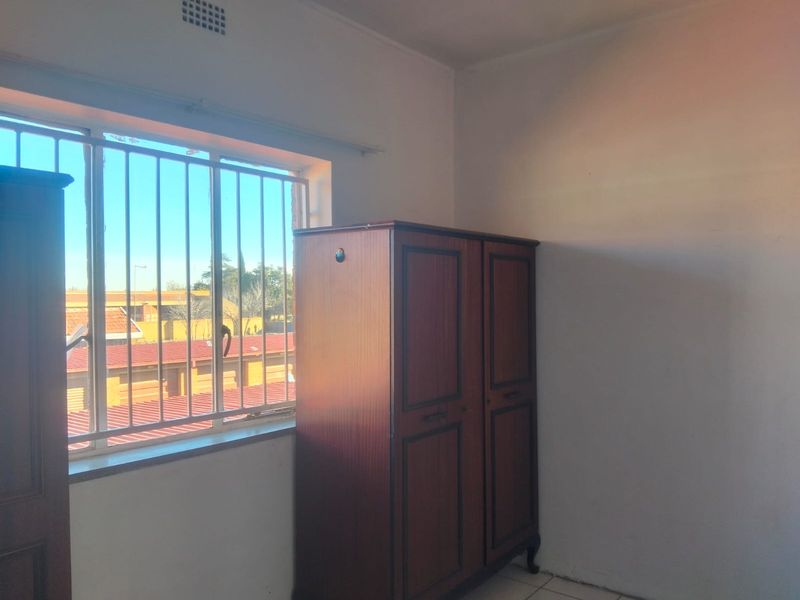 A bedroom featuring tiled flooring and a window fitted with security bars, offering a functional space with natural light.