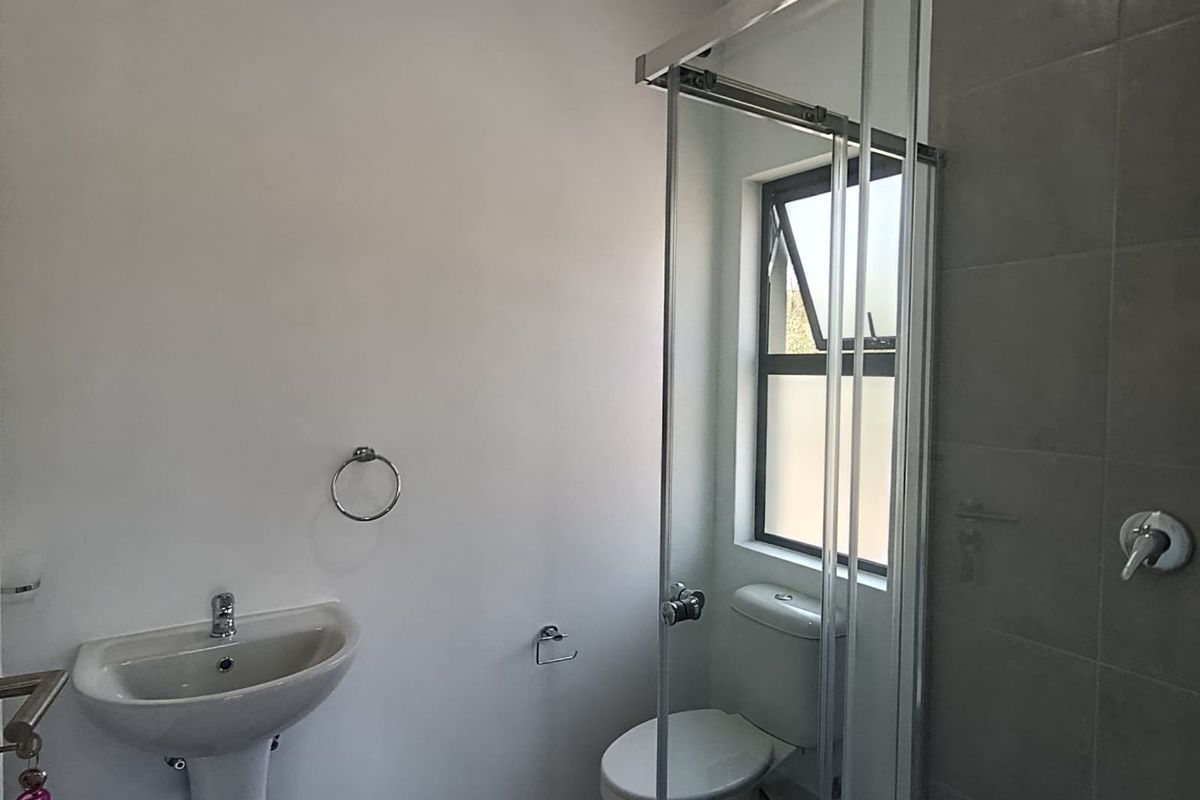 A clean, modern bathroom featuring a pedestal basin, a toilet, and a glass-enclosed shower with grey wall tiling.