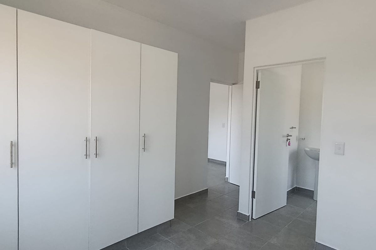 A clean, empty bedroom featuring modern grey floor tiles, built-in white cupboards, and direct access to an en-suite bathroom.
