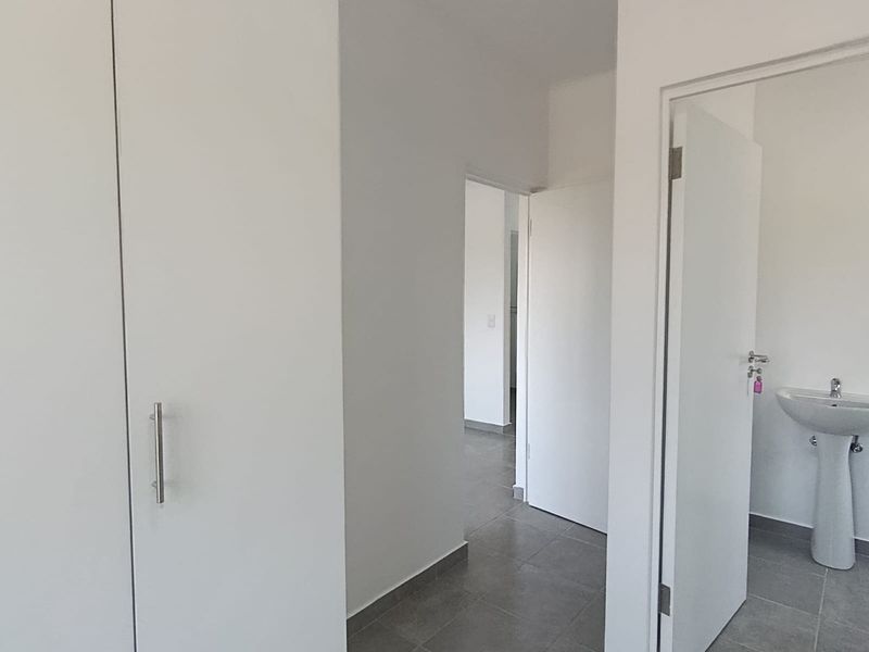 A clean, minimalist hallway featuring tiled flooring, built-in storage cupboards, and access to an adjacent bathroom with a pedestal basin.