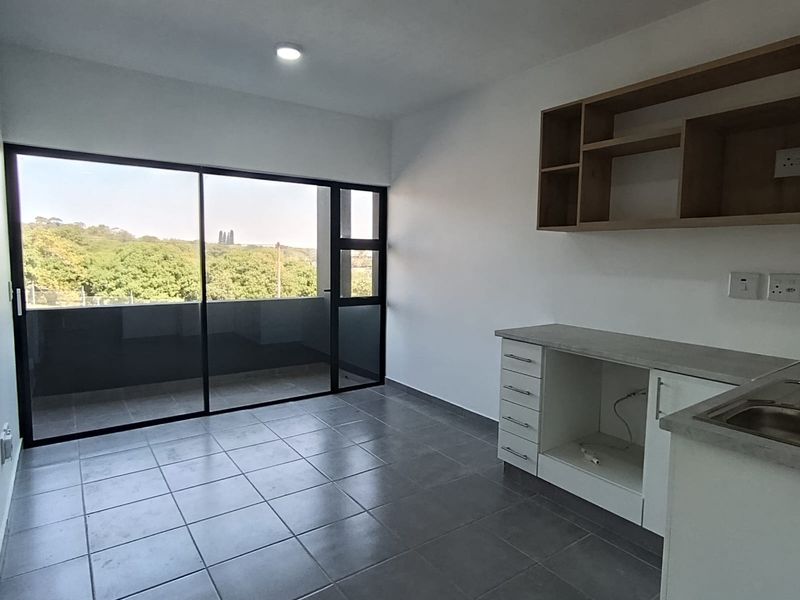 An open-plan living and kitchen area featuring tiled floors, built-in cabinetry, and a large sliding door leading to a balcony with scenic views.