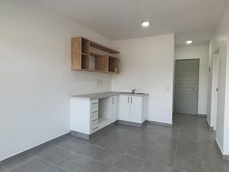 A clean, modern kitchen area featuring white base cabinetry, wood-tone open shelving, a stainless steel sink, and neutral grey floor tiles.