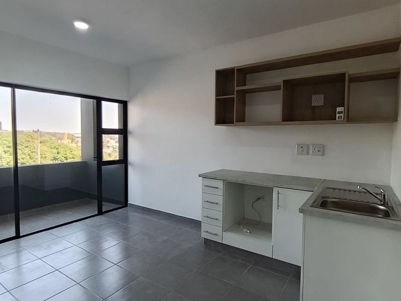 A modern, empty kitchen area featuring tiled floors, built-in cabinetry with open shelving, a stainless steel sink, and access to a private balcony.