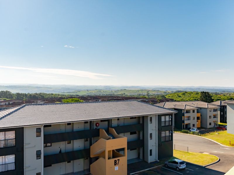 Elevated view overlooking the apartment complex, surrounding residential area, and distant landscape.