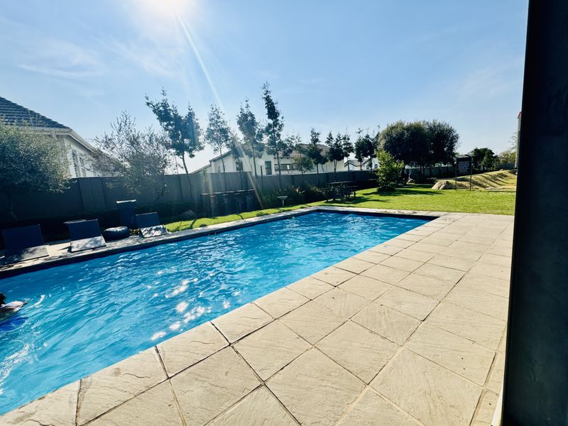 A well-maintained outdoor swimming pool area featuring a paved deck, surrounding lawn, and boundary wall, perfect for relaxation and outdoor recreation.
