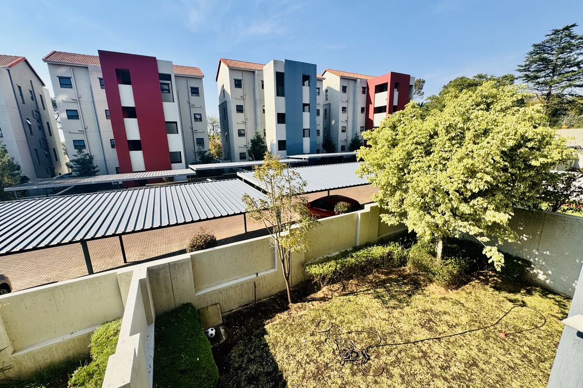 An elevated view of a residential complex featuring a private garden area, concrete boundary walls, and covered carport parking bays.