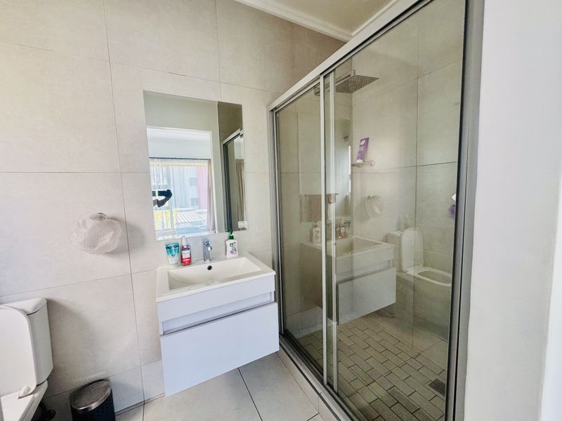 Modern bathroom featuring a wall-mounted vanity, basin, and a spacious glass-enclosed shower with a rain shower head and neutral wall tiling.