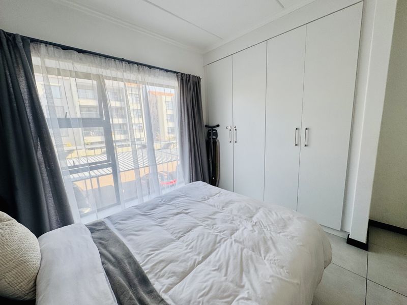 A bright bedroom featuring neutral tiled flooring and ample built-in cupboard storage with modern finishes.