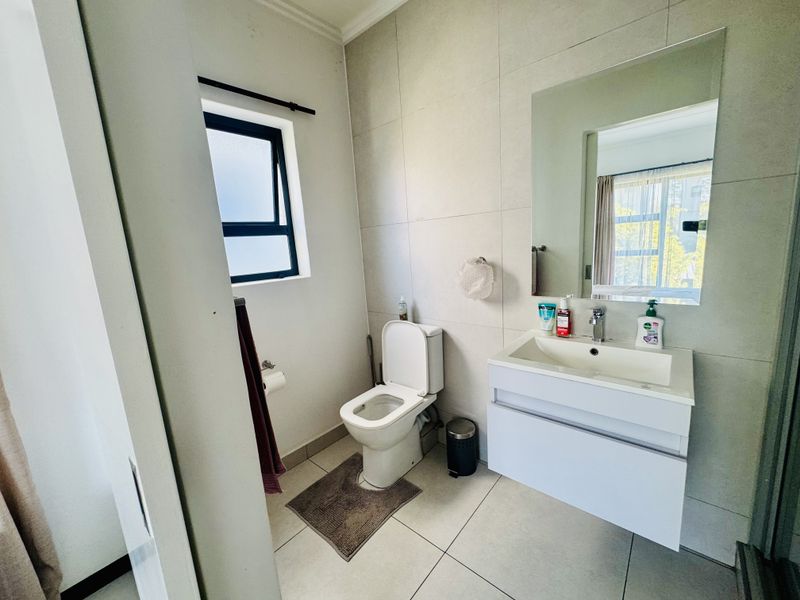Modern bathroom featuring a wall-mounted vanity with a ceramic basin, large mirror, tiled finishes, and a top-hung window for natural light.