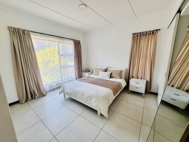 A bright and spacious bedroom featuring large windows, neutral tiled flooring, and a built-in wardrobe.