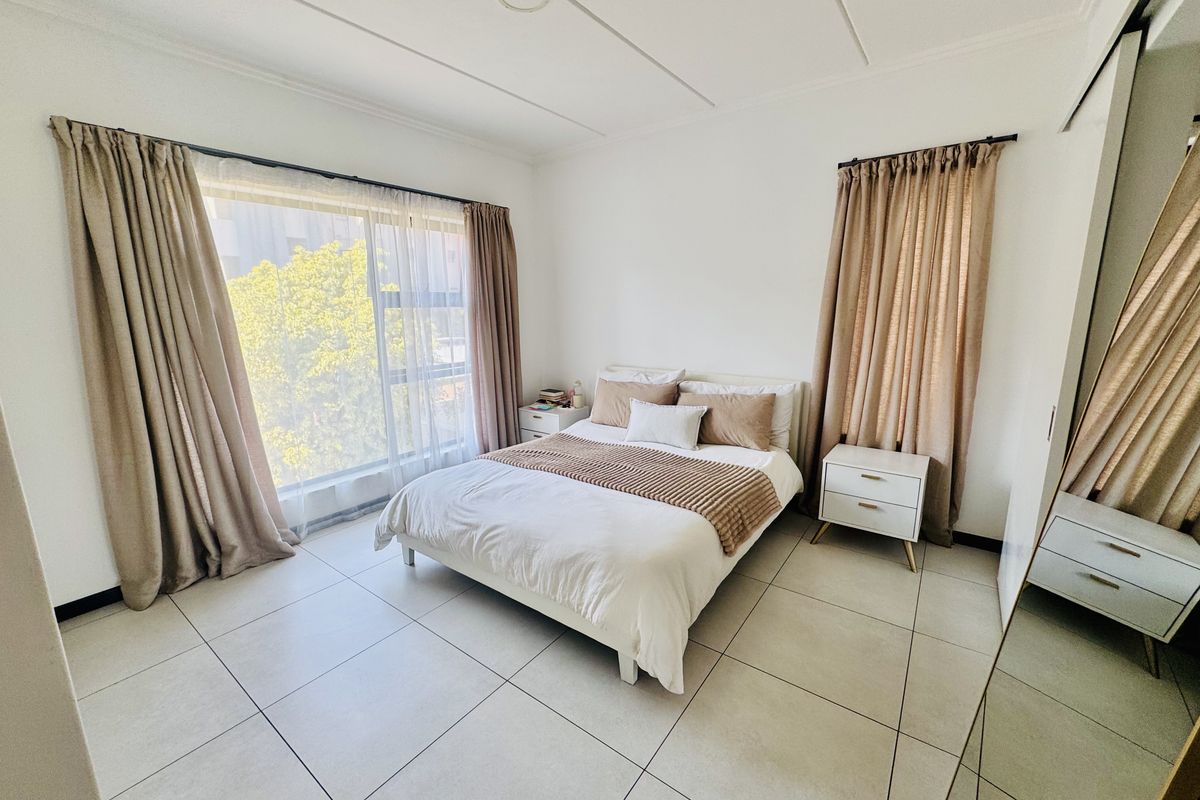 A bright and spacious bedroom featuring large windows, neutral tiled flooring, and a built-in wardrobe.