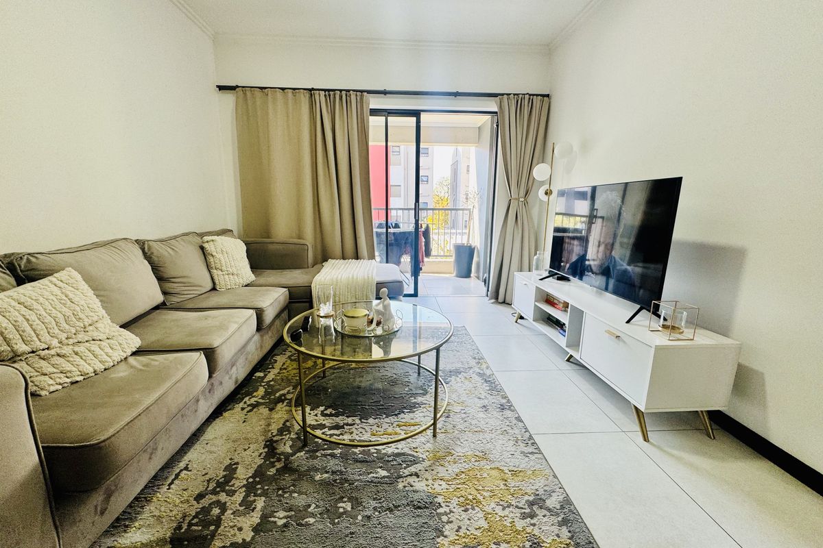 A well-maintained living room featuring neutral tiled flooring and a sliding glass door providing access to an outdoor balcony area.