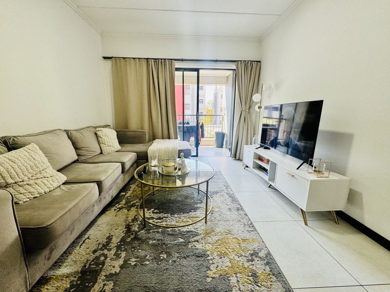 A well-maintained living room featuring neutral tiled flooring and a sliding glass door providing access to an outdoor balcony area.