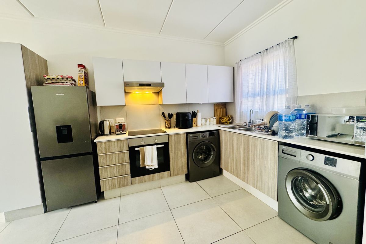 Modern kitchen featuring light wood-grain cabinetry, sleek countertops, integrated oven and hob, and tiled flooring, offering a functional and contemporary cooking space.
