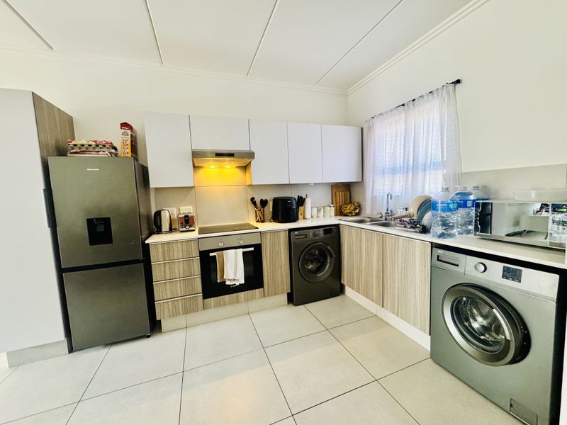 Modern kitchen featuring light wood-grain cabinetry, sleek countertops, integrated oven and hob, and tiled flooring, offering a functional and contemporary cooking space.