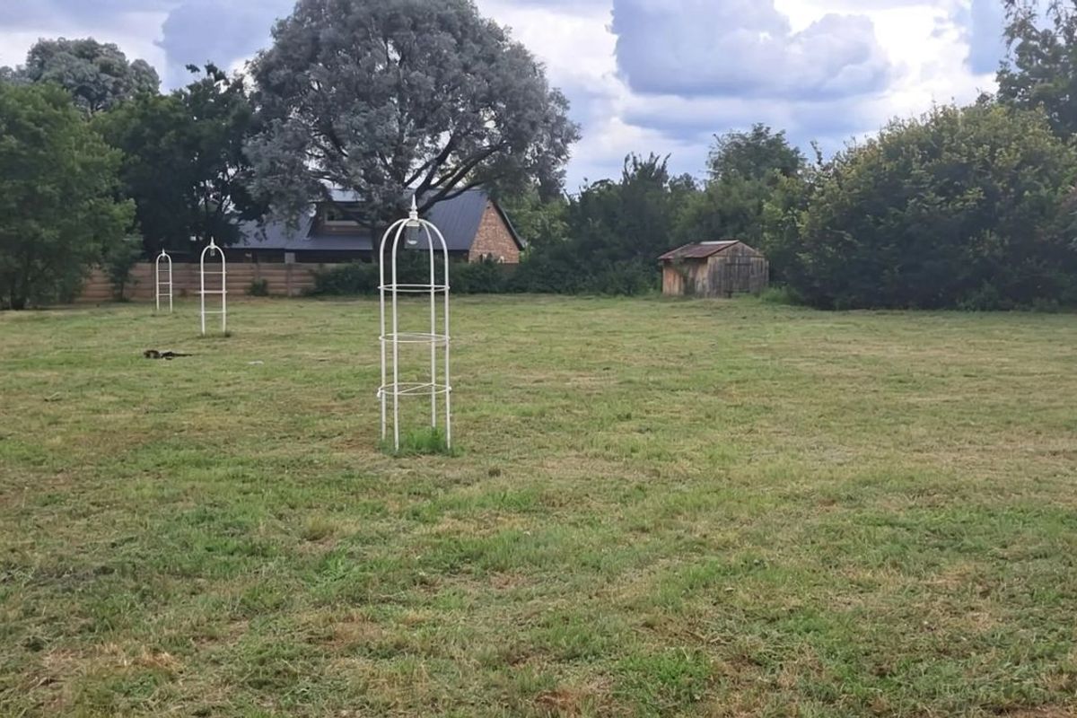 A spacious residential vacant land plot featuring established trees, metal garden trellises, and a small wooden storage shed.