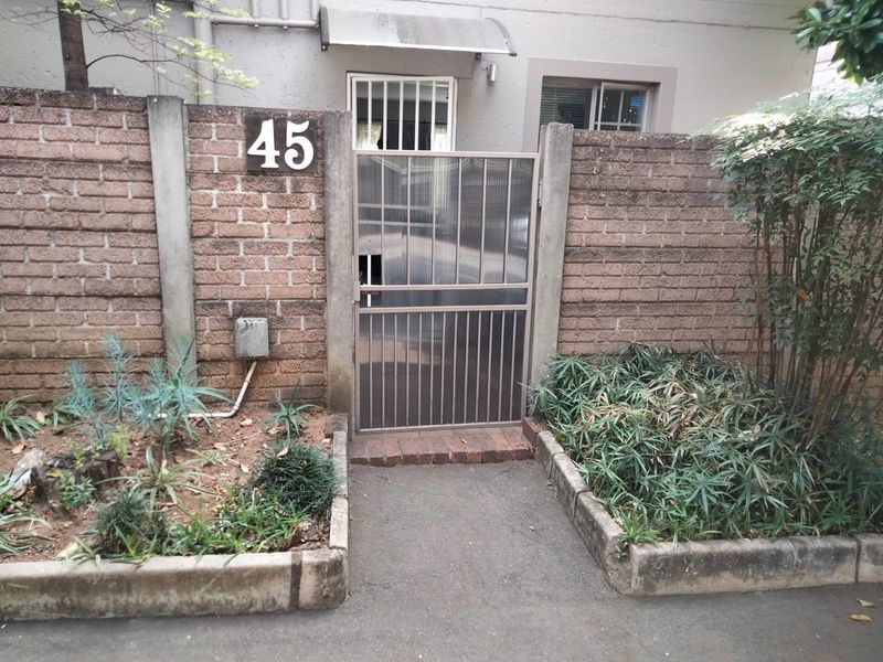 Front entrance of the townhouse featuring a brick boundary wall, metal security gate, and a small paved walkway.