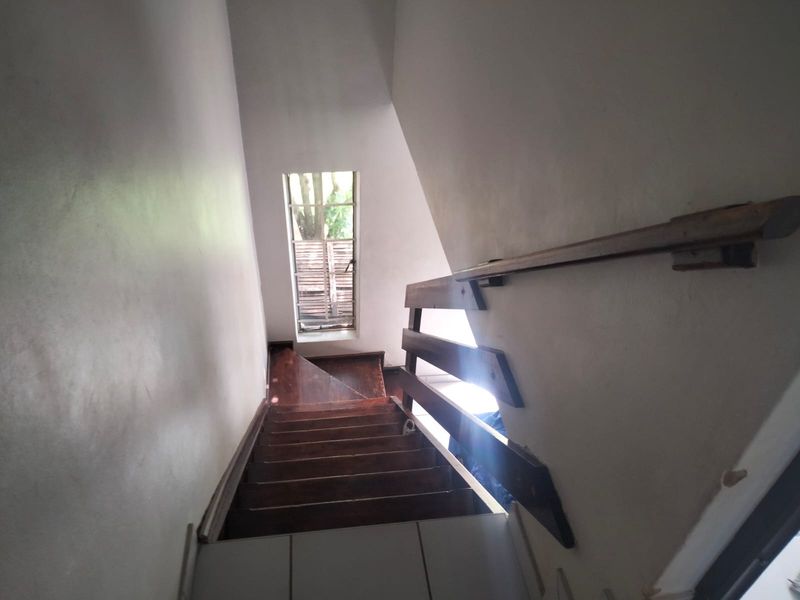 A view looking down a wooden staircase with a timber handrail, featuring a window at the landing and plain white walls.