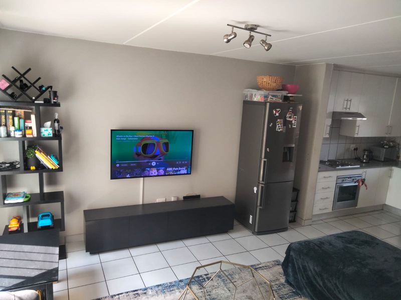 Open-plan living area featuring tiled flooring, track lighting, and a functional kitchen with built-in oven, hob, and extractor fan.