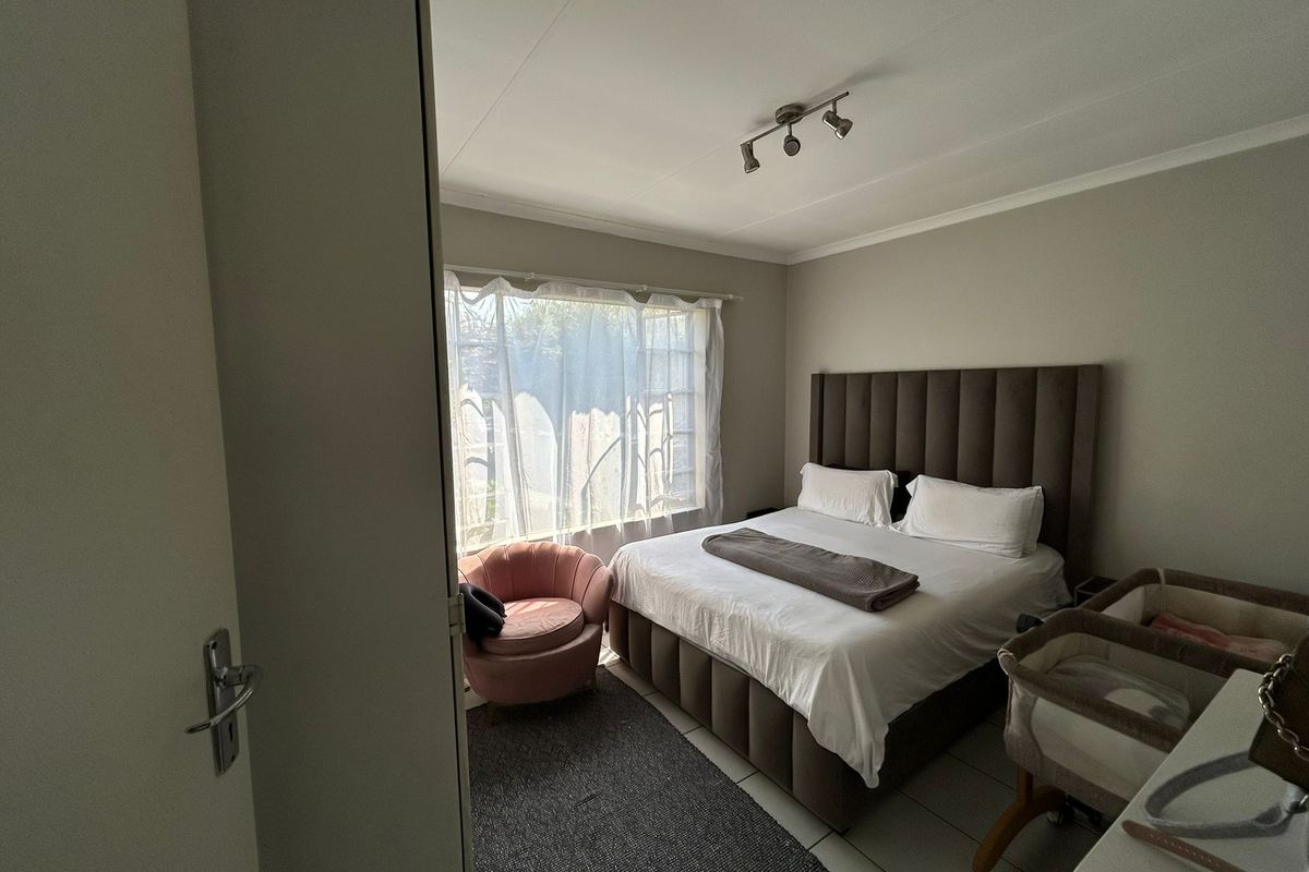 A functional bedroom featuring tiled flooring, neutral wall tones, and a window fitted with a security gate.