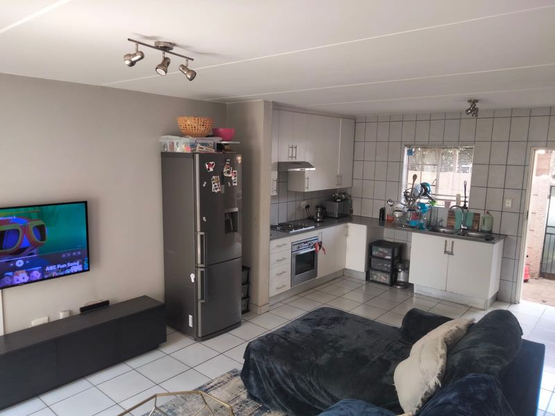 Open-plan living and kitchen area featuring tiled flooring, built-in cabinetry, integrated oven and hob, and direct access to an outdoor space.