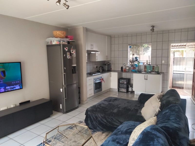 Open-plan living area featuring a functional kitchen with built-in cabinetry, oven, hob, and tiled finishes, seamlessly connected to the lounge space.